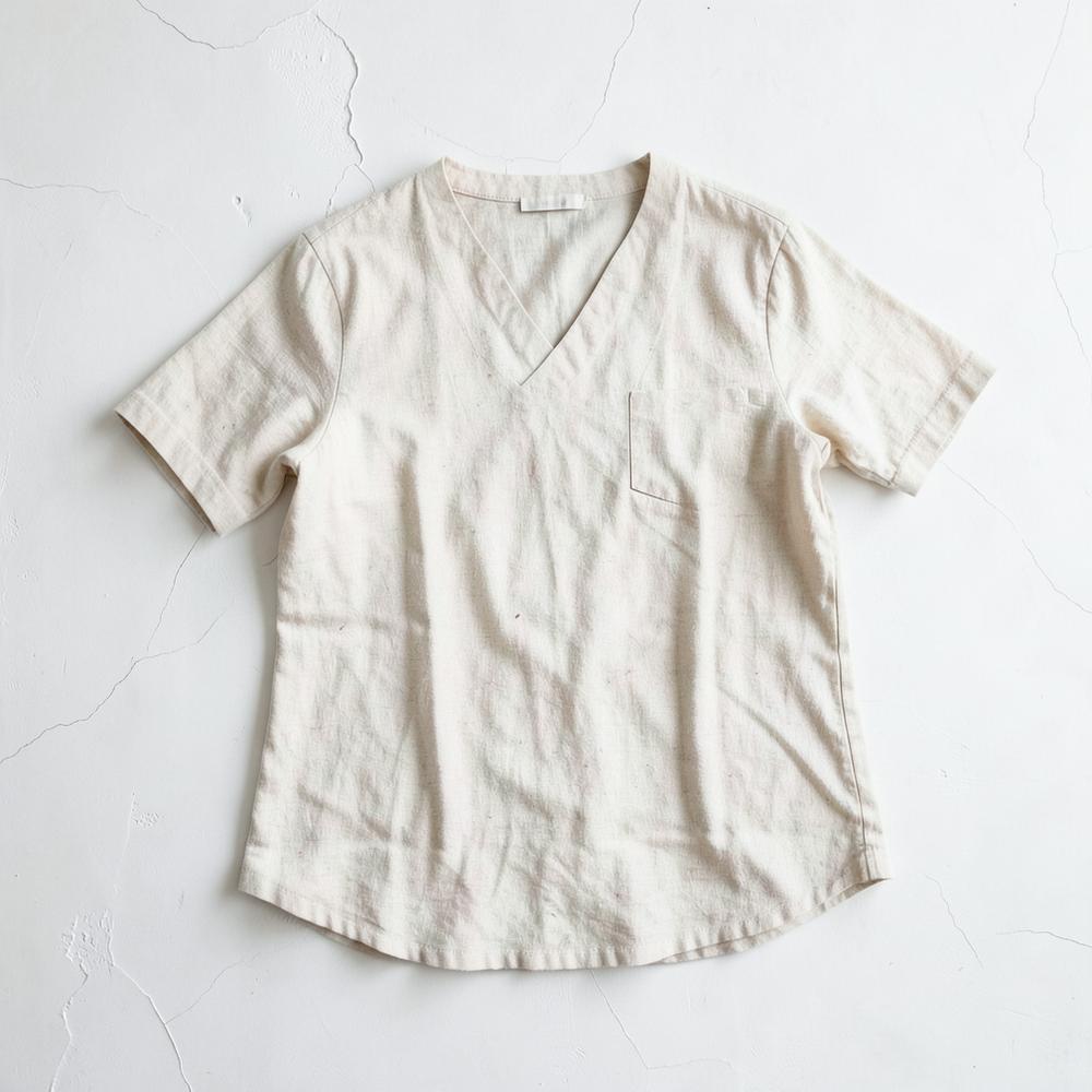 Manteau de lin non teint posé à plat sur un fond blanc cassé, lumière diffuse.