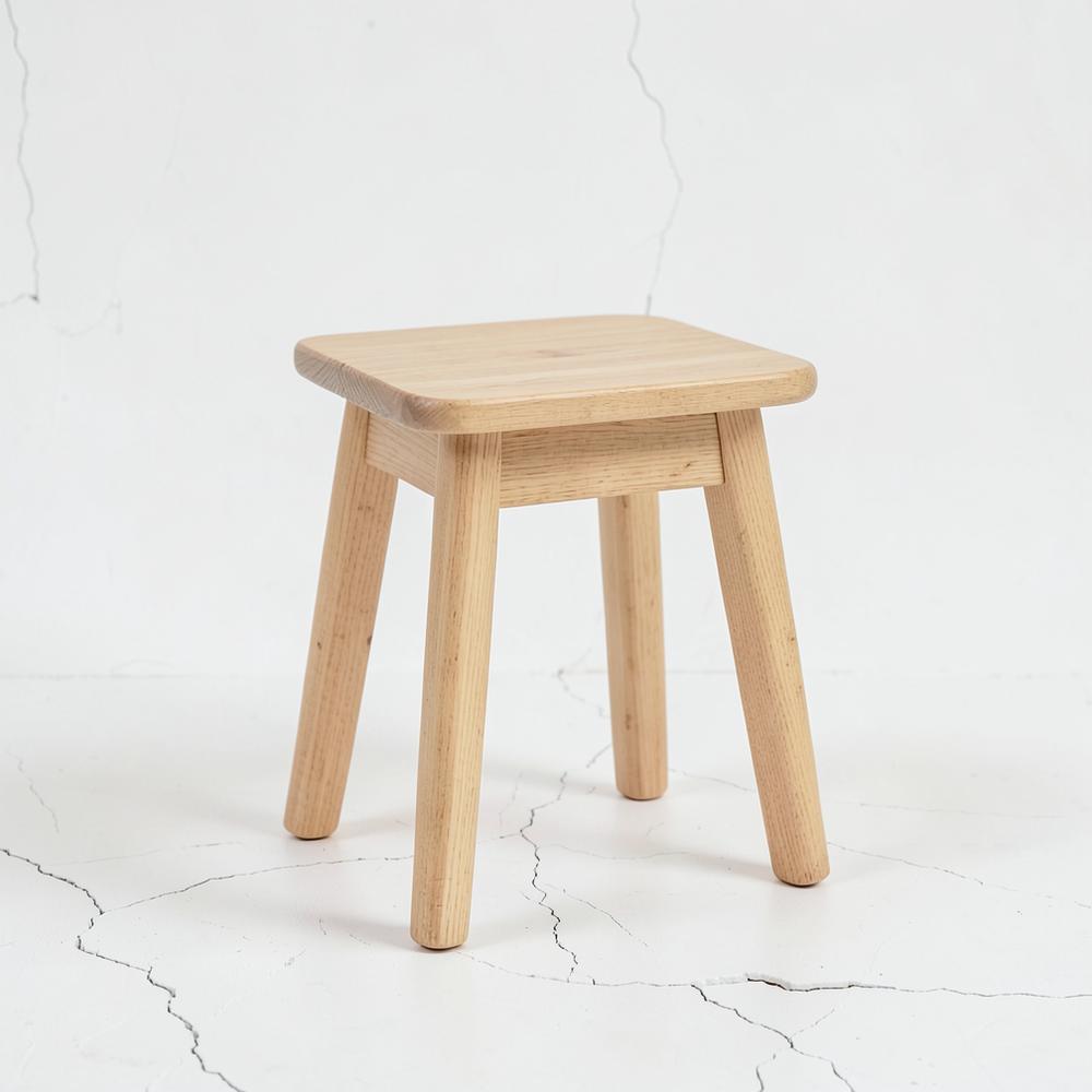 Tabouret en frêne clair non verni, vue de trois quarts, fond neutre.